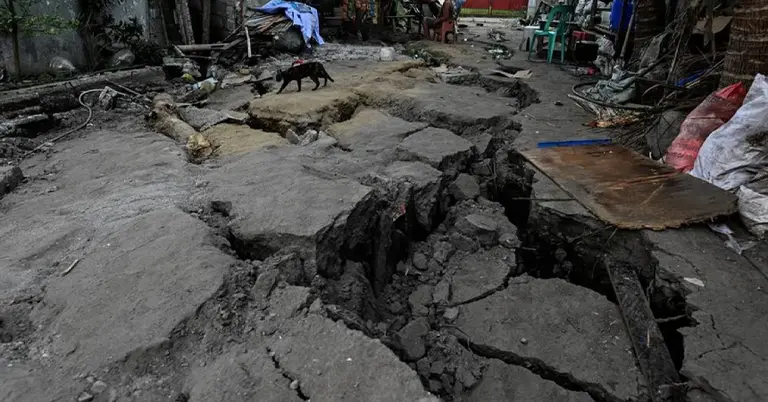 ভূমিকম্পের পরের দিন ফাটল ধরা একটি রাস্তার পাশে নিজেদের বাড়ির সামনে বসে আছেন কিছু মানুষ